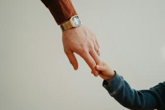 a person holding the hand of a child by Andrik Langfield courtesy of Unsplash.